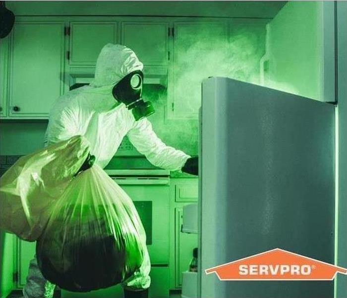 Green tinted photo of a person in a hazmat suit holding closed garbage bags reaching in to an open fridge
